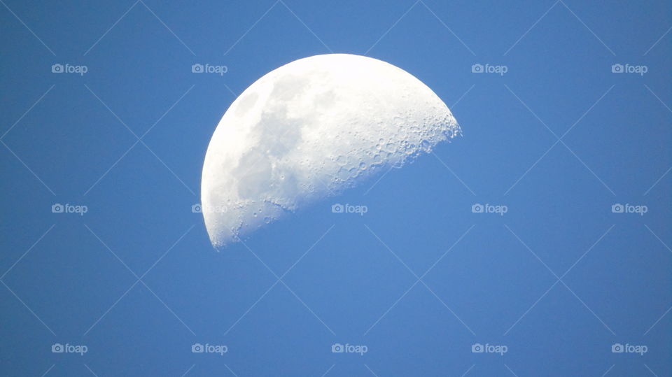 Closeup craters half moon during day against bright blue sky one heart shaped crater on horizon