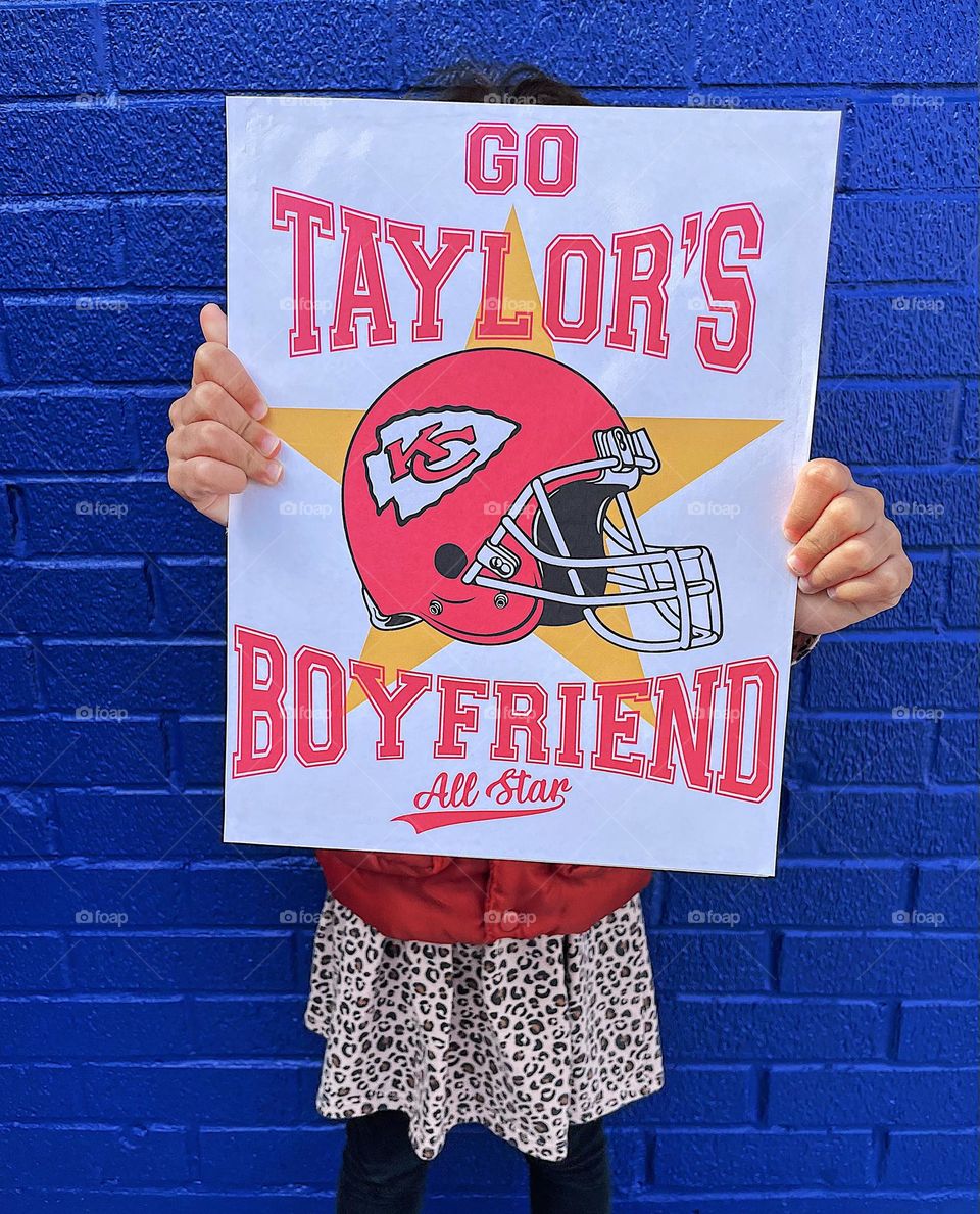 Toddler holds funny sign, go Taylor’s Boyfriend sign, making signs for the Super Bowl, funny signs 