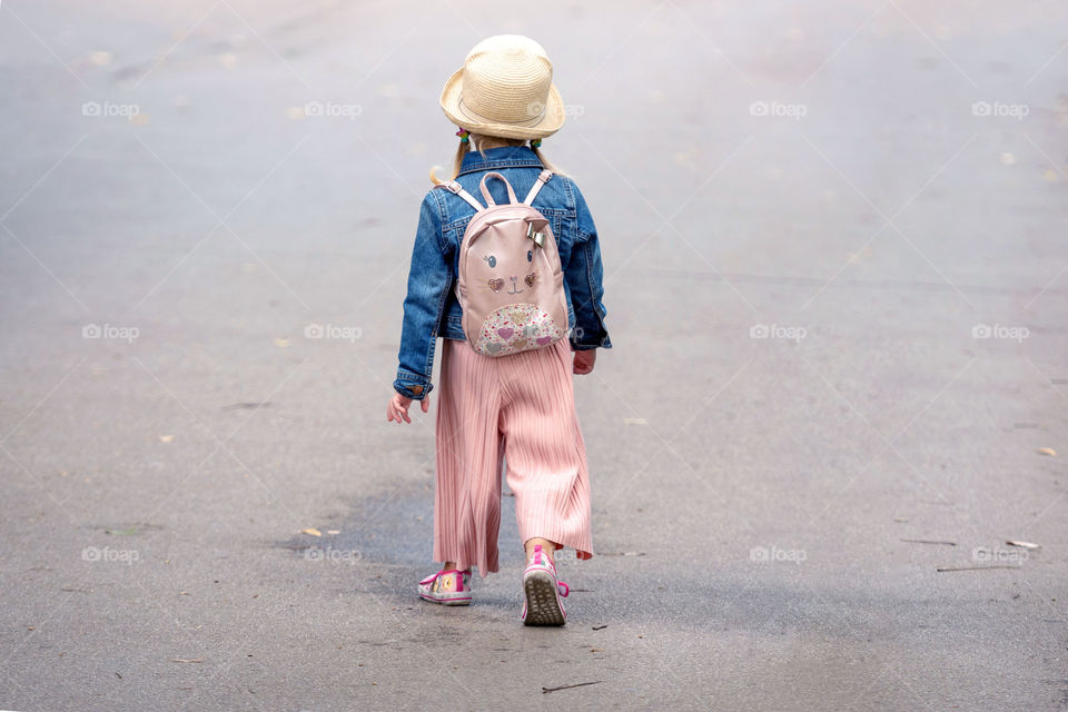 a little girl with backpack going along the sidewalk, rear view