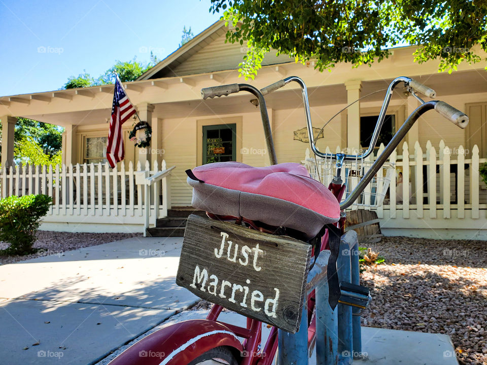 A vintage bicycle with a Just Married sign sits in front of a classic single family home