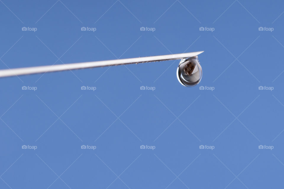 Close-up or macro of syringe needle with a drop at the tip on a blue background . 
reflection of pills in a drop. Hospital, health, care, doctor, injection, vaccine, vaccination, illness, disease