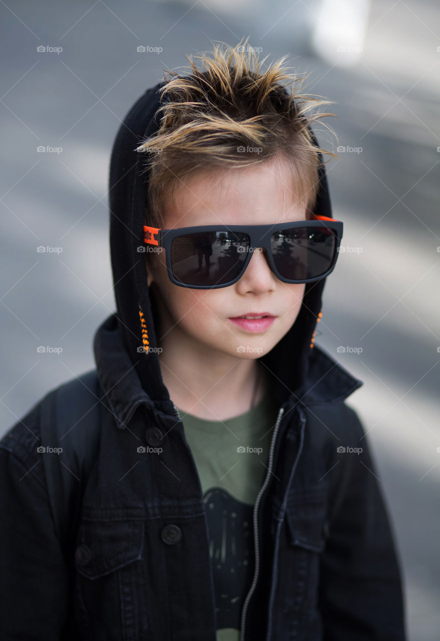 stylish boy in black clothes and glasses is walking along the street.  baby five years old, beautiful blond