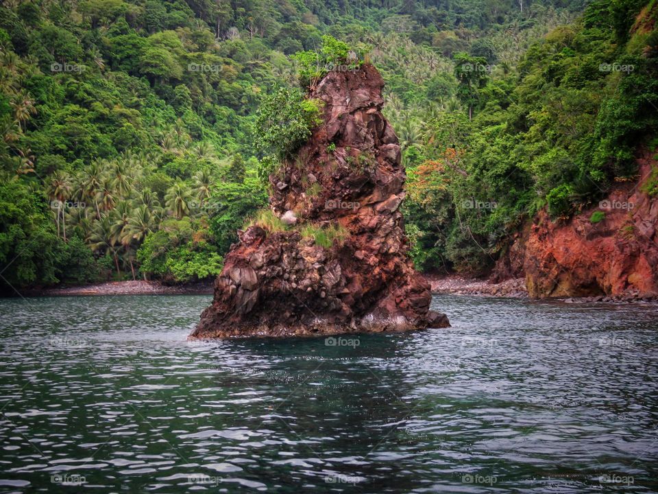 Nature landscape, a small rock island against a backdrop of hills and green trees.