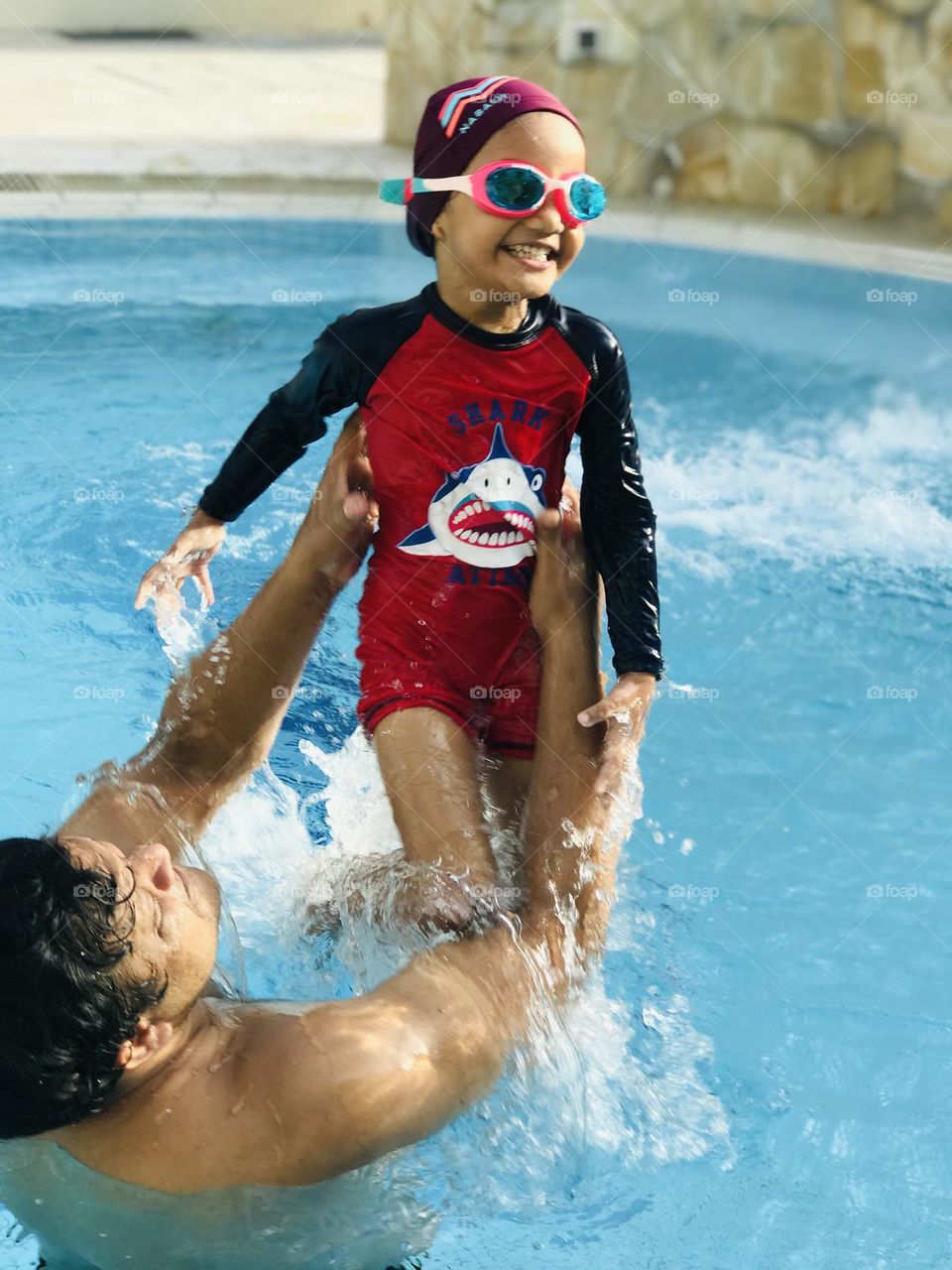 A father and daughter enjoying and smiling a lot at swimming pool.