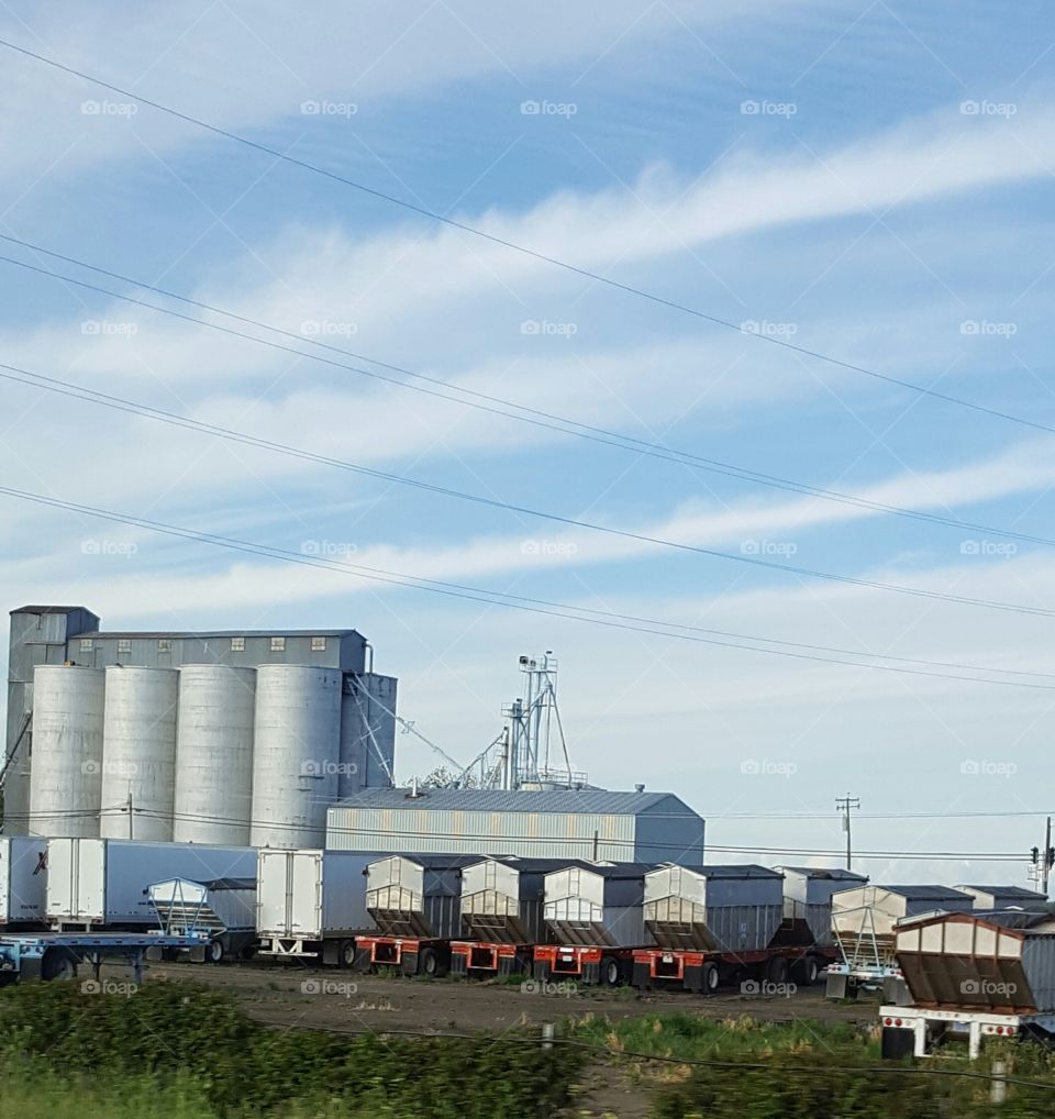 trucks lined up along silos as the sun is setting along a California highway.