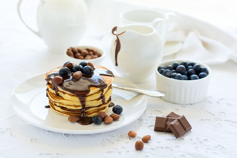 Stack of pancakes with chocolate sauce, blueberries and nuts