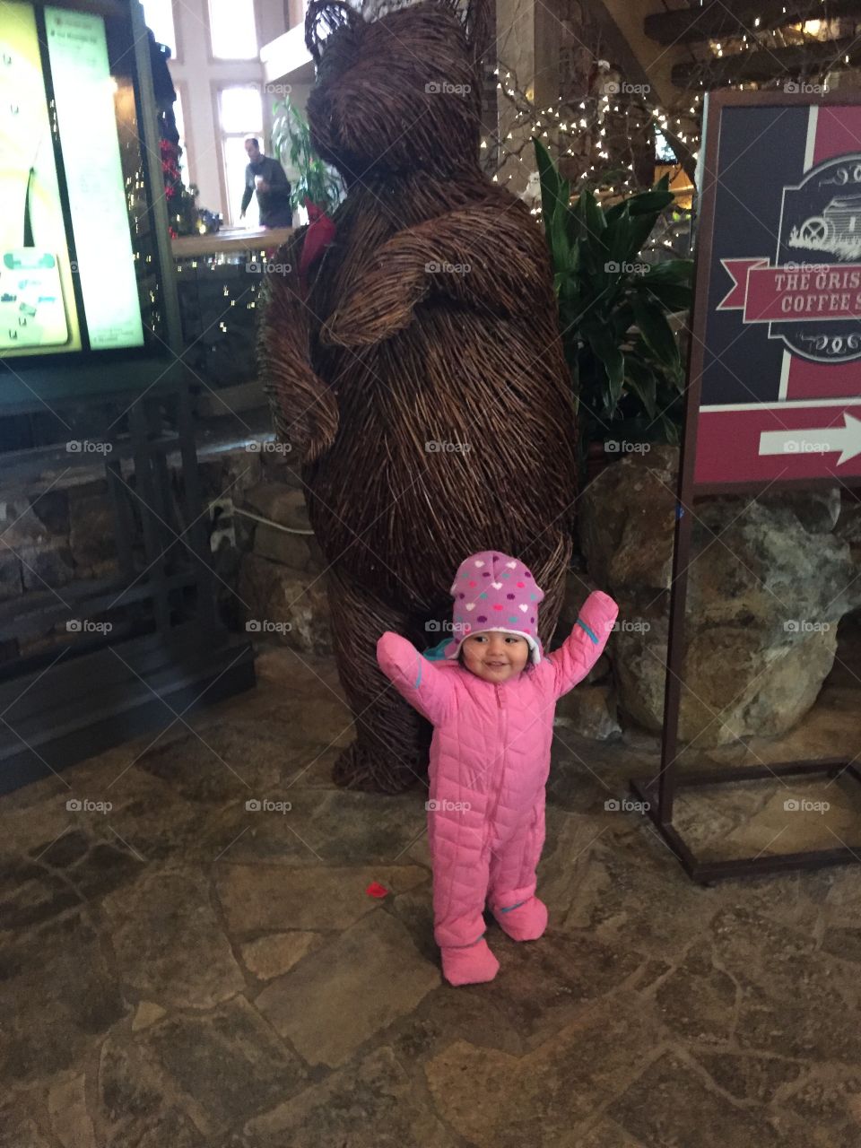 My baby in a winter snow suit next to a wooden statue of a bear 