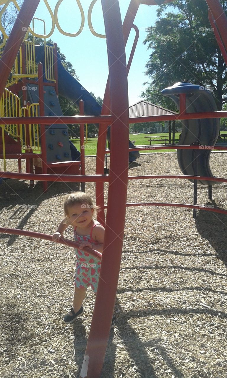 Playful Girl. peering happily at me through the playground equipment!