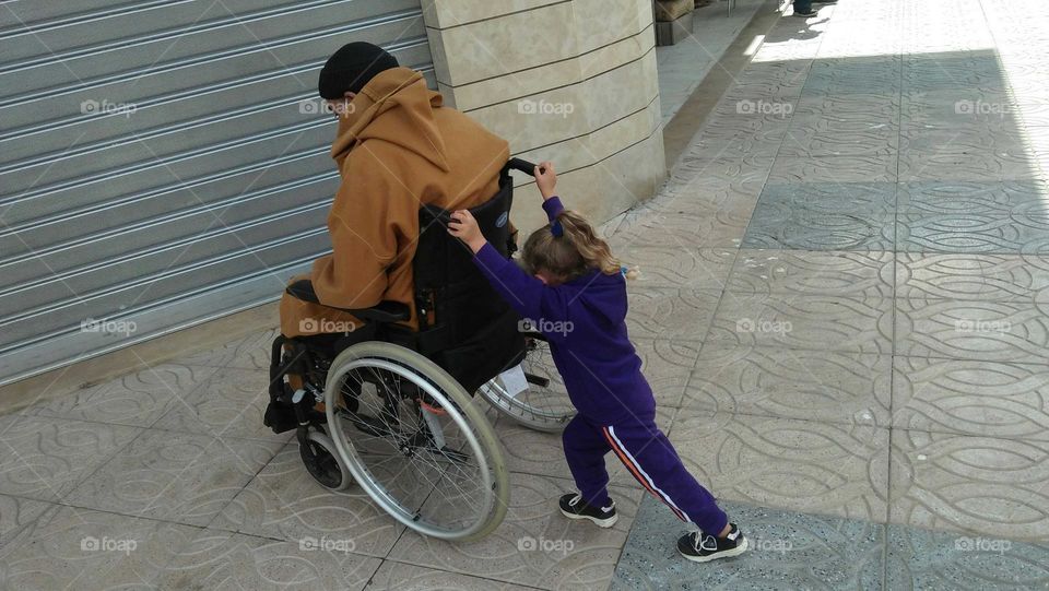 Brave child angel  MALAK helps her disabled father by pushing his wheelchair