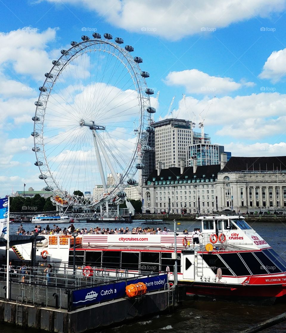 sunny day in london showing london eye and tourist boat on river thames
