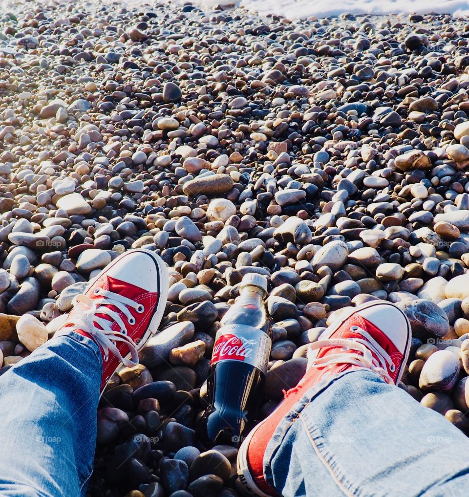 A bottle of Diet Coke on the beach with red sneakers.