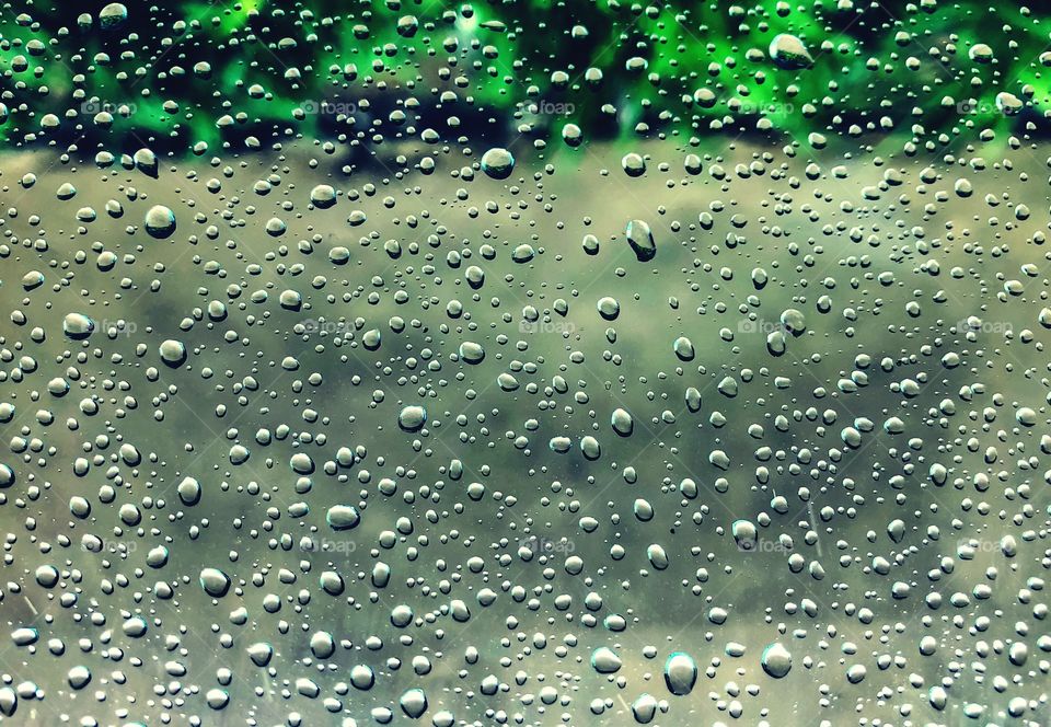 Raindrops against a car window- raindrops that look like bubbles in water in beautiful green hue water