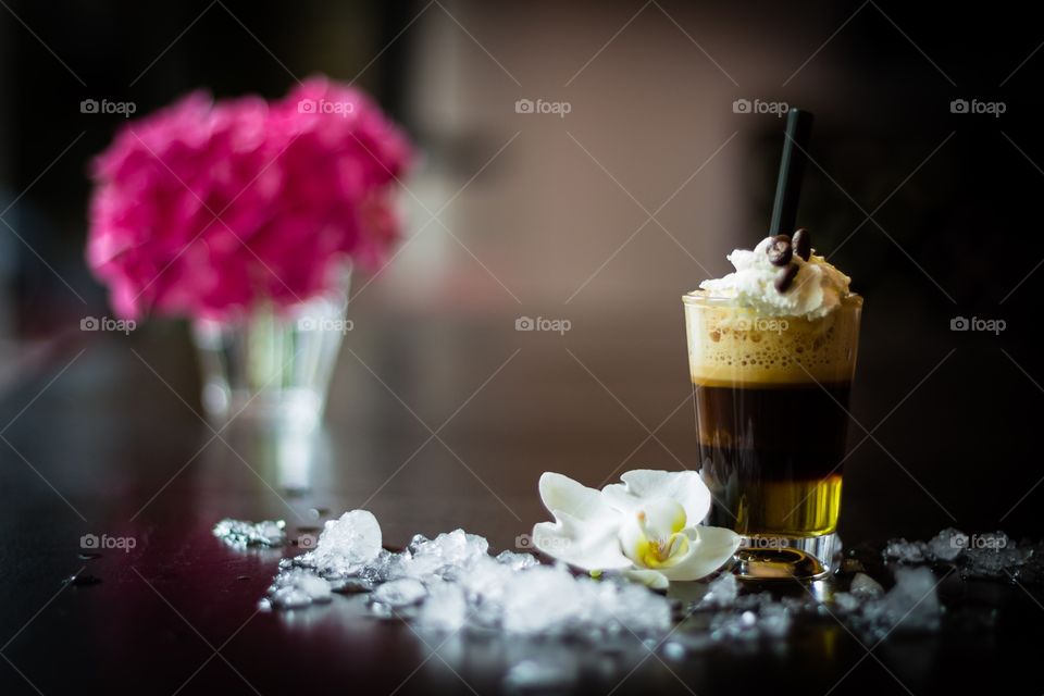 Espresso macchiato decorated with ice cubes and flowers on wooden café table