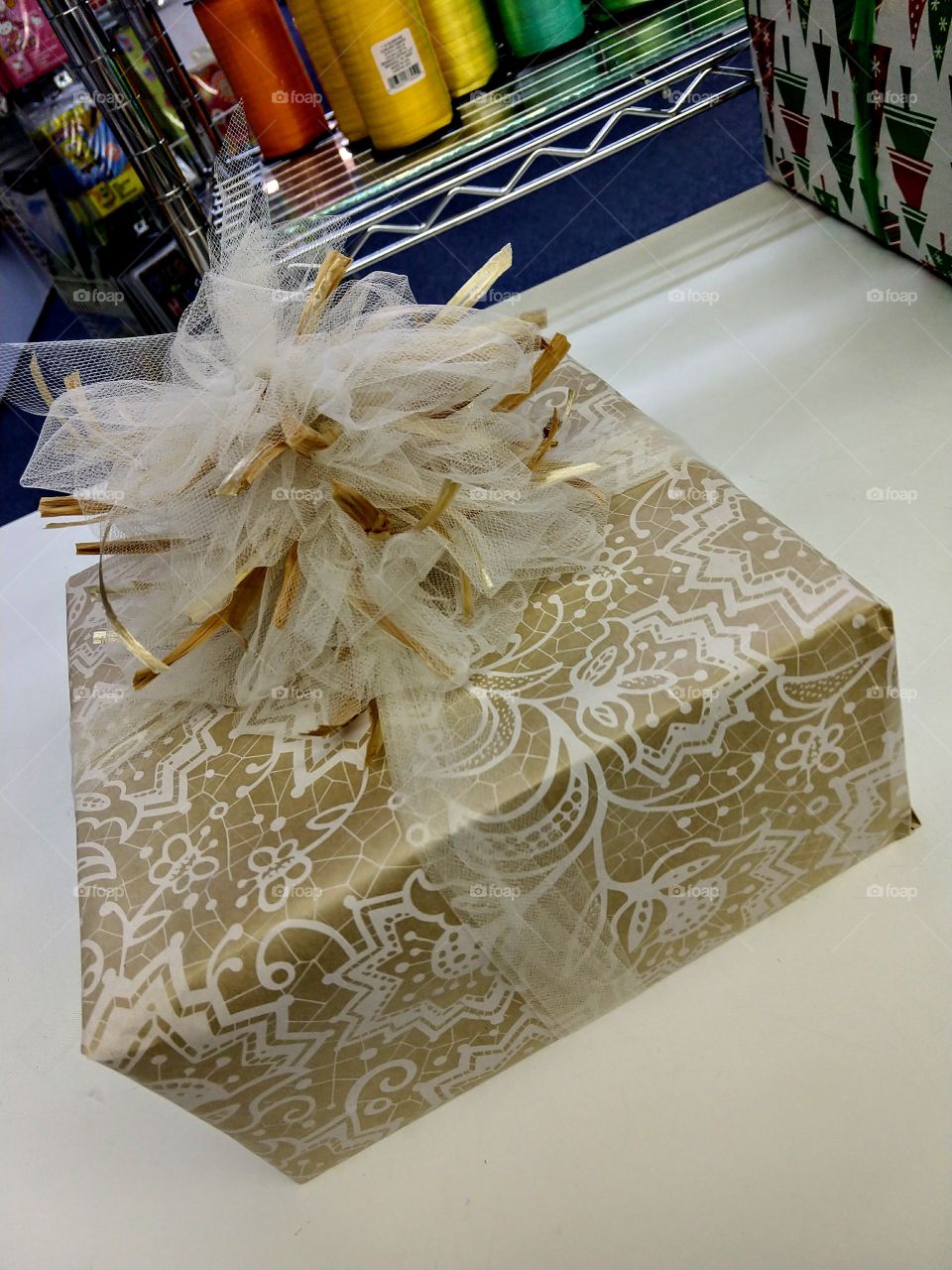 handwrapped gift done in a beige and white lace type wrapping paper with a tulle and raphia bow