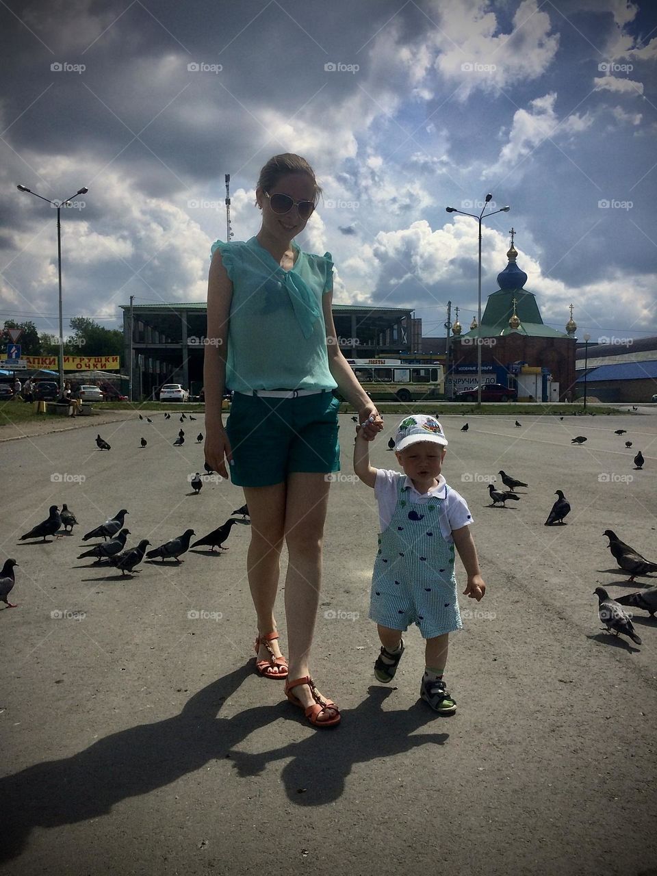 Mom and child are walking in the city park around a lot of pigeons