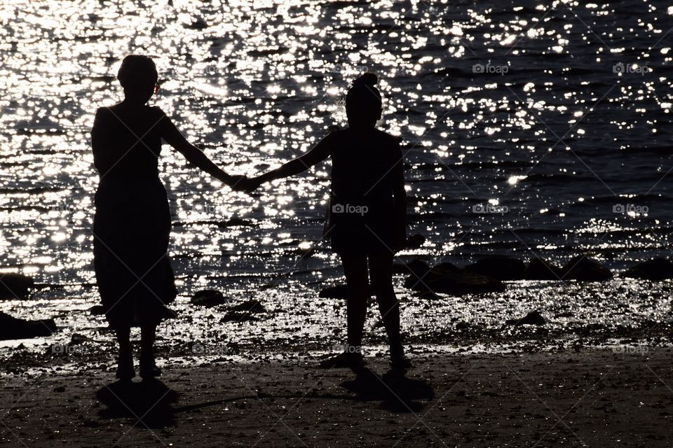 Silhouette of two people walking by water 