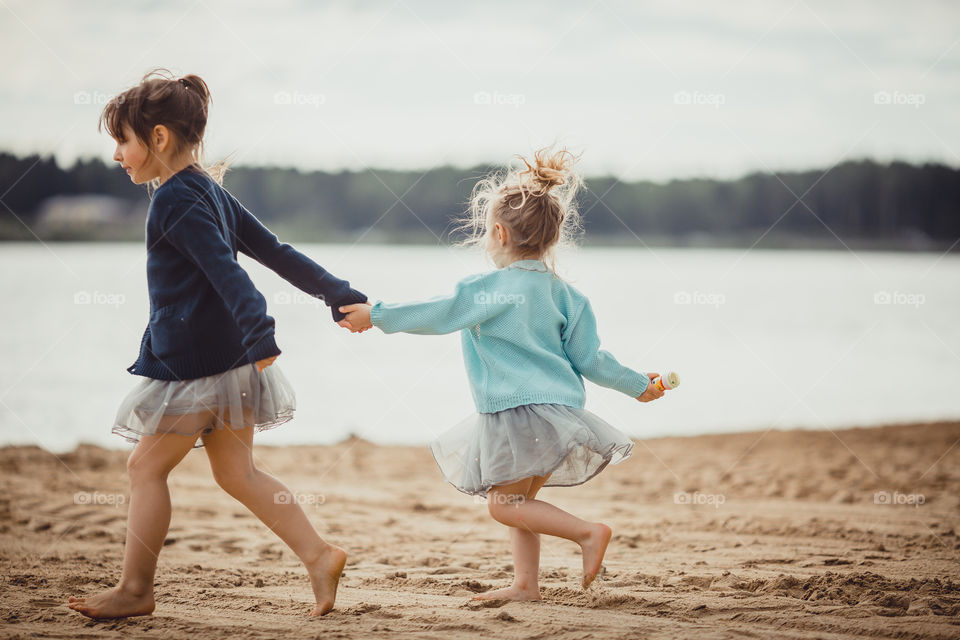 Little sisters on lake coast at sunny evening. 