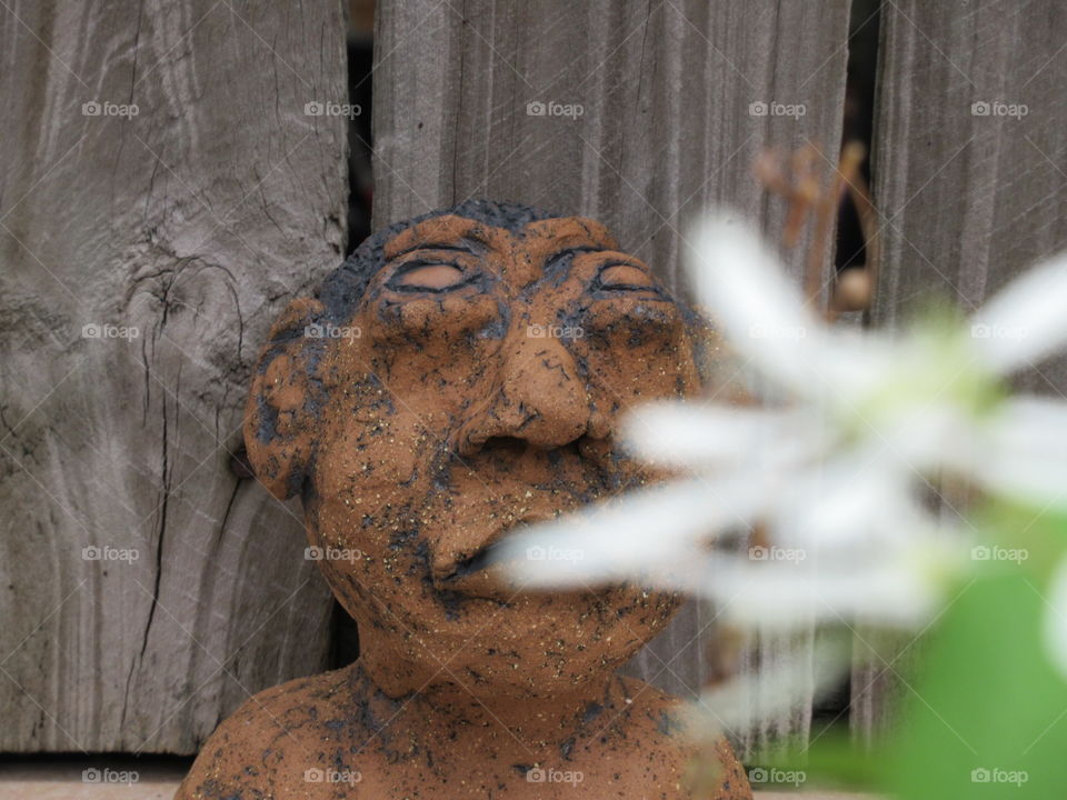 A clay figure the was hand created contrasting to the white life of a flowing plant