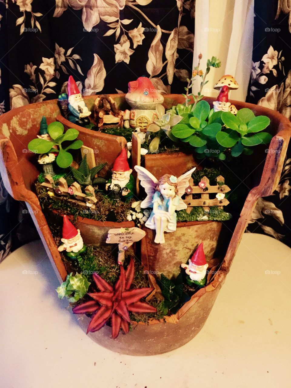 Creative plant life and fairy tale nic nacs mixed together in a broken clay pot