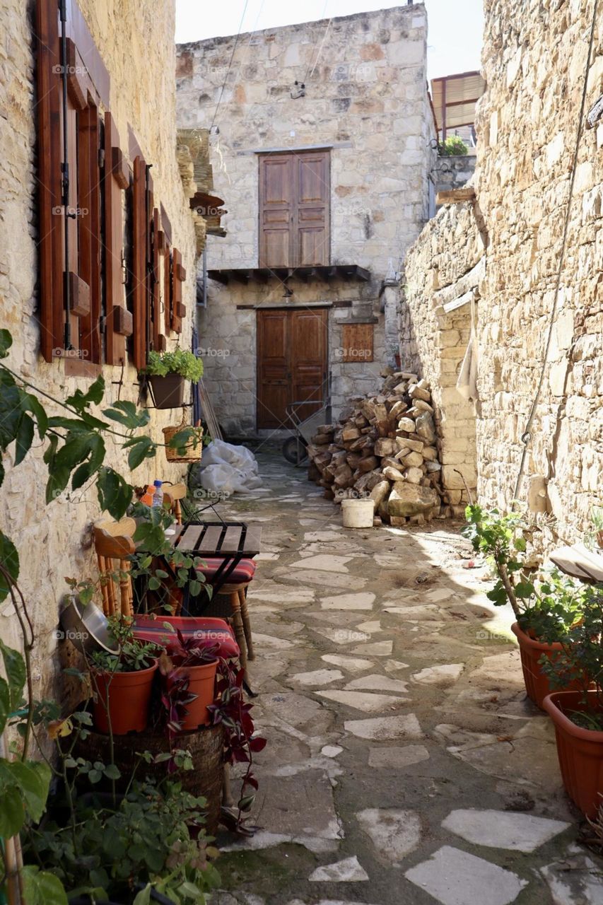 Little alley in old village with plants pots and a bench with stone walls and path