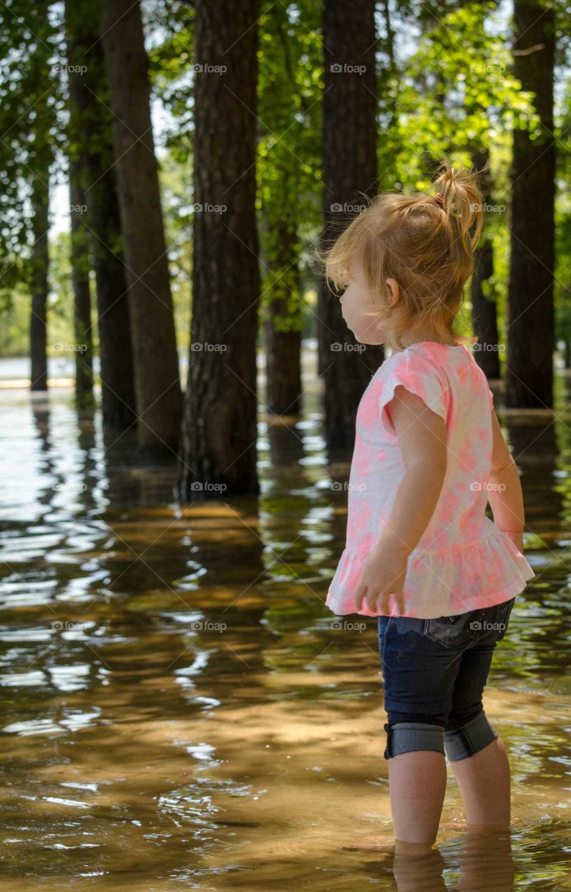 Little girl standing near lake in forest