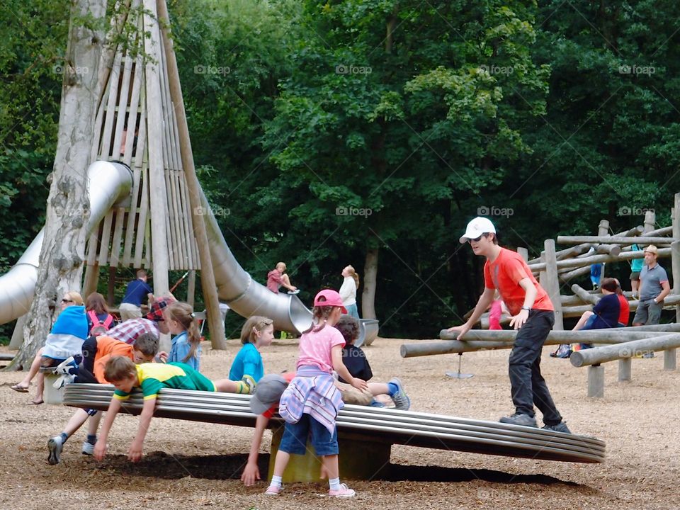 Children sitting, standing, and laying on a merry-go-round while they play at a public park on a summer day. 