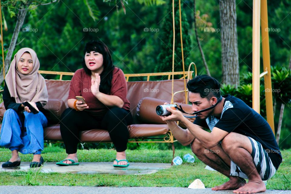 an asian man aims at an object while squatting in a park.