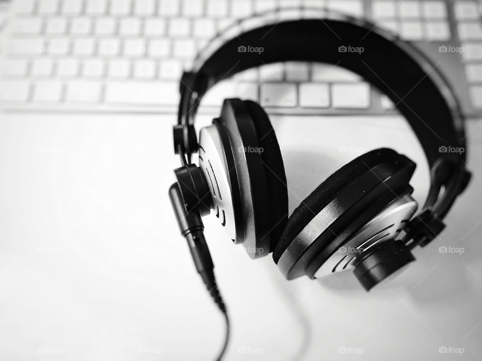 Black and white professional headphones with blurred computer keyboard in background. Selective focus. Music and relaxation concept 