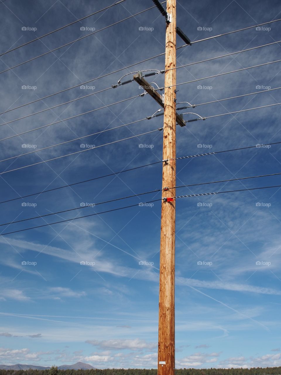 A power pole in rural Central Oregon stands tall against a rich blue sky with forest and mountains in the background on a sunny spring day. 
