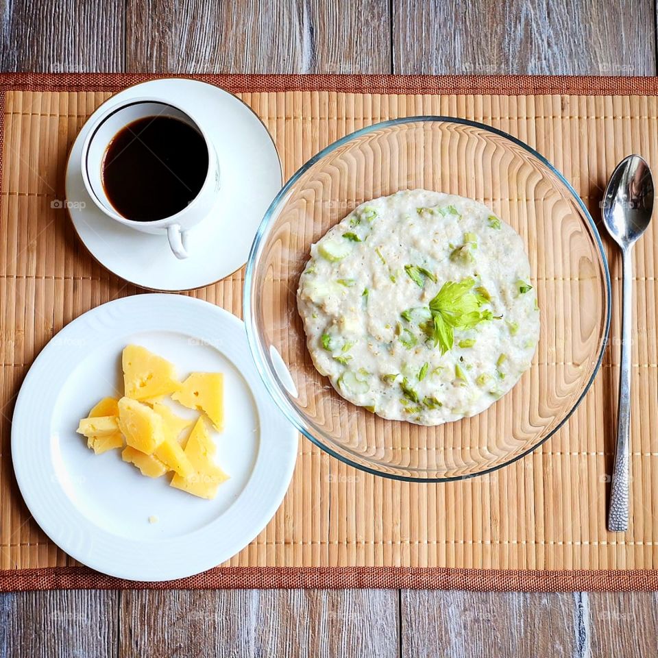 Breakfast.  Oatmeal with a mix of fruits, a plate of cheese and a cup of coffee.  Nearby lies a metal spoon