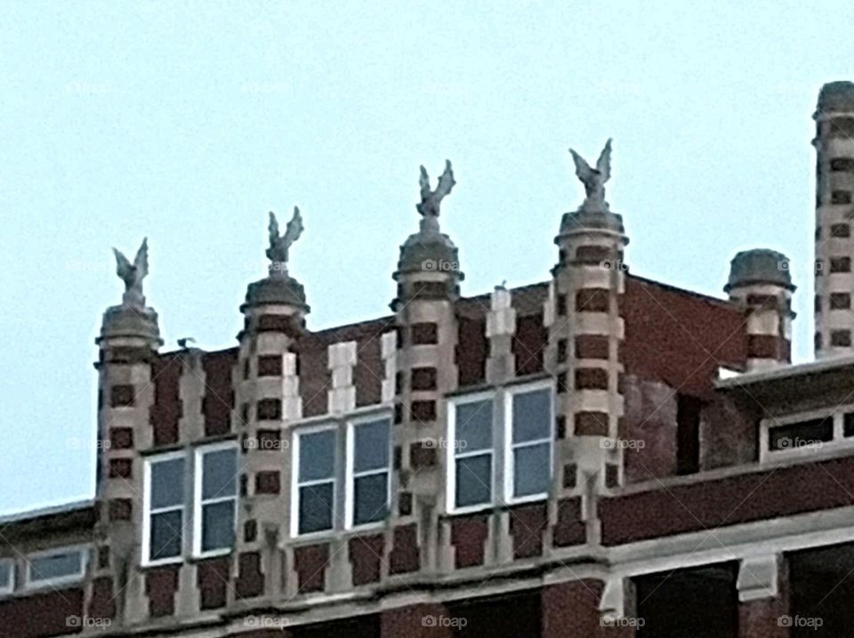 A creepy brick building with windows and four gargoyles on top at dawn