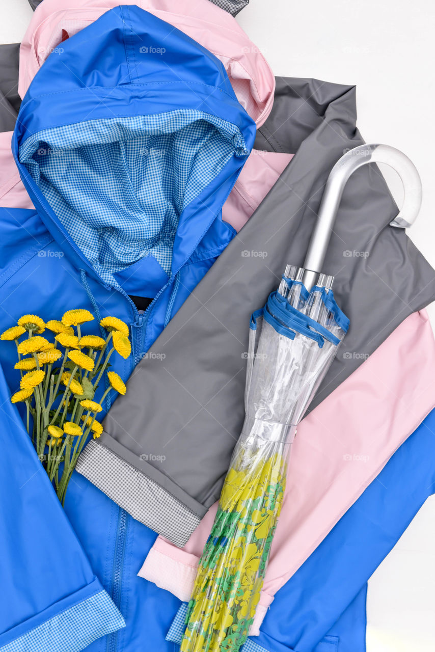 Flat lay of different colored raincoats with a bouquet of flowers and an umbrella