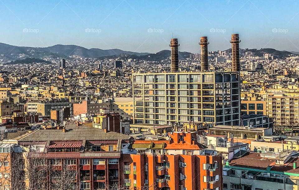 A view of the city of Barcelona, with the 3 Chimneys and a sprawl of offices and apartments blocks that spread on for miles towards the mountains in the far distance 