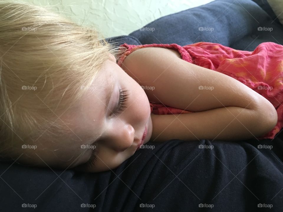 Sleeping baby girl with blonde hair wearing a pink dress.