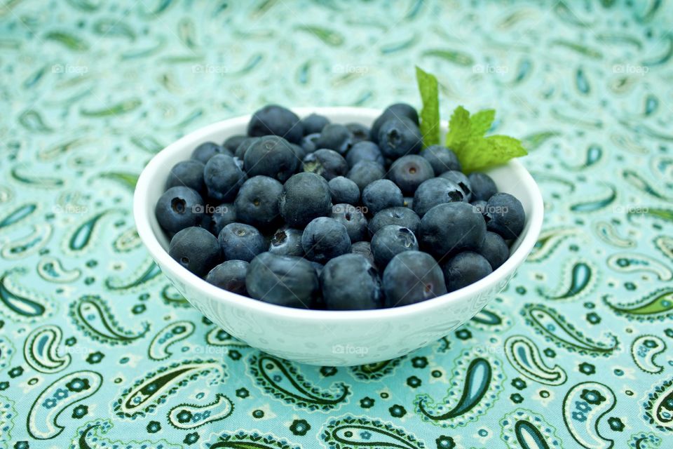 Fruits! - Blueberries and a spring of mint in a white bowl on teal and green paisley fabric