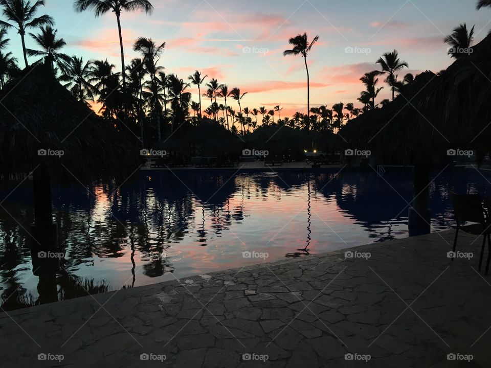 Beautiful sunset with the silhouette of palm trees by a swimming pool