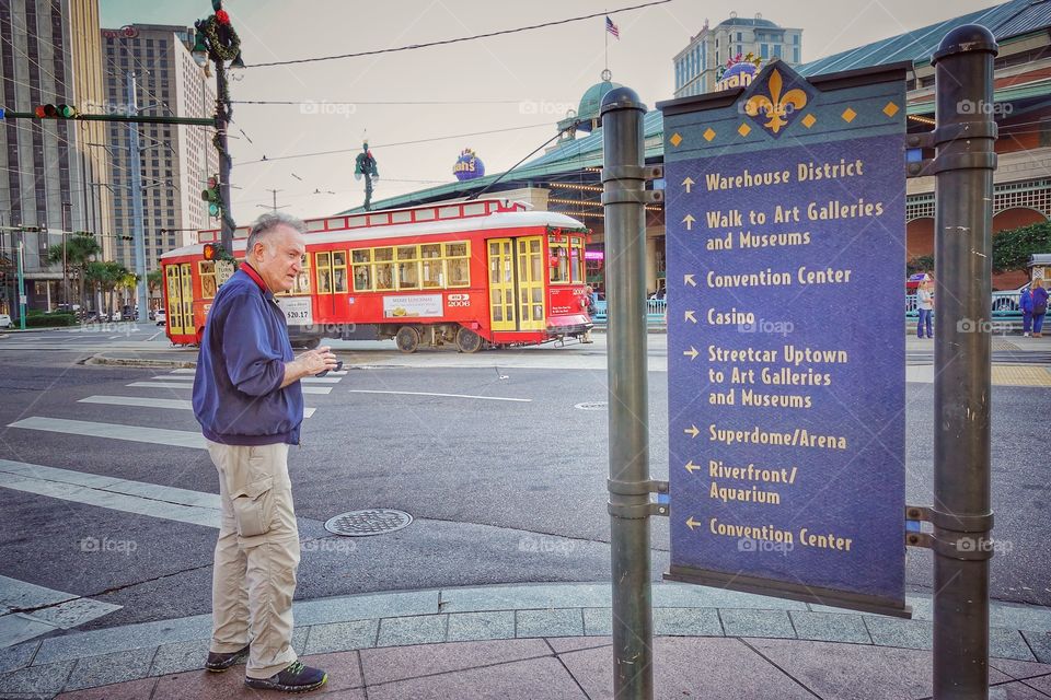 A visitor looking at the directory board. A vintage tram passes by in the background. At the French Quarter, New Orleans, Louisiana, USA.