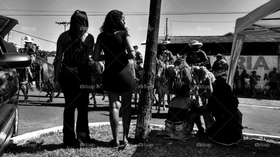 Pessoas na cidade em confraternização, cavalgada nas ruas. Homens e mulheres. Jovens e crianças. Desfile com animais; cavalos,  burros, bois/touros e veículos. Cowgirls, cowboys...