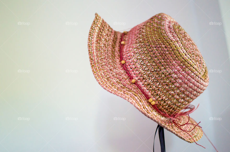 Pink straw fedora hat on white background hanging on hat rack 