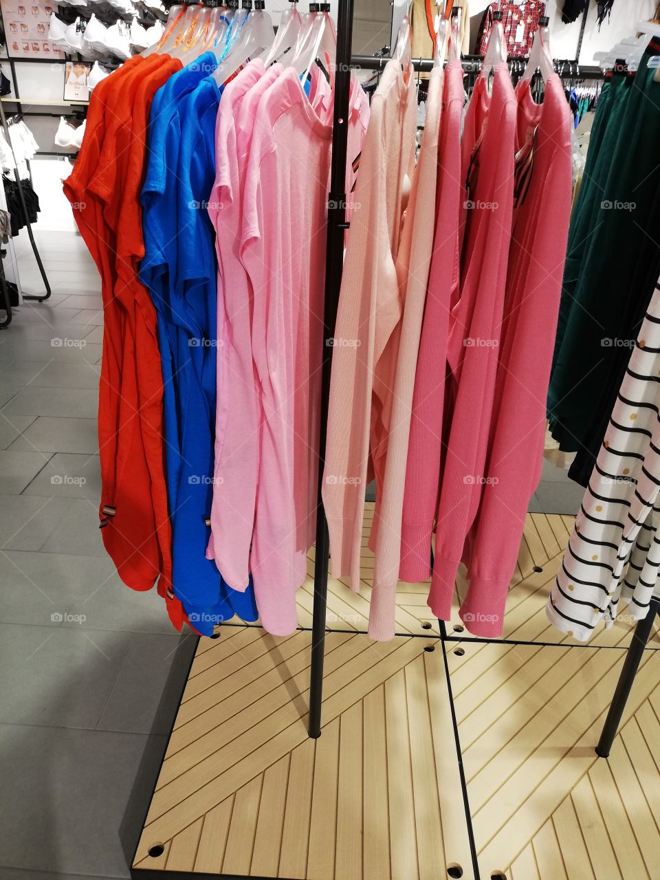 Plenty of different colors nightdresses and striped pants are hanging on the hangers on the rack, sizes are seen above the clothes. In the background white bras are shown in the bright light.