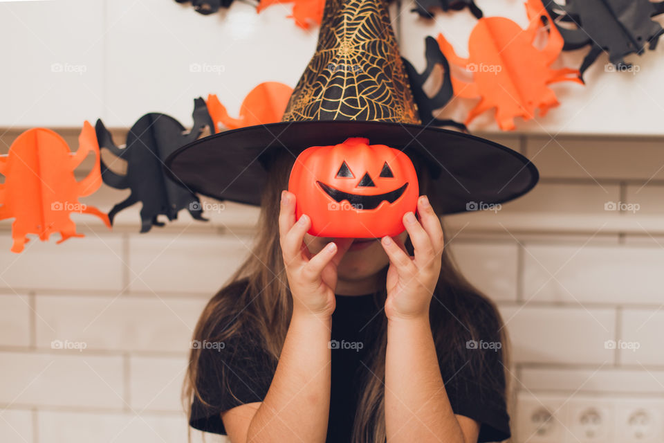 Little girl dressed as a witch for halloween holding a pumpkin with a face on the background decor