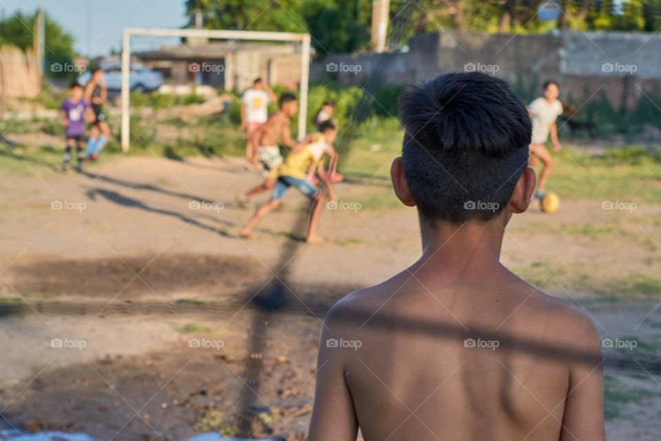 children playing ball on a dirt court. Photo seen from behind the goal.