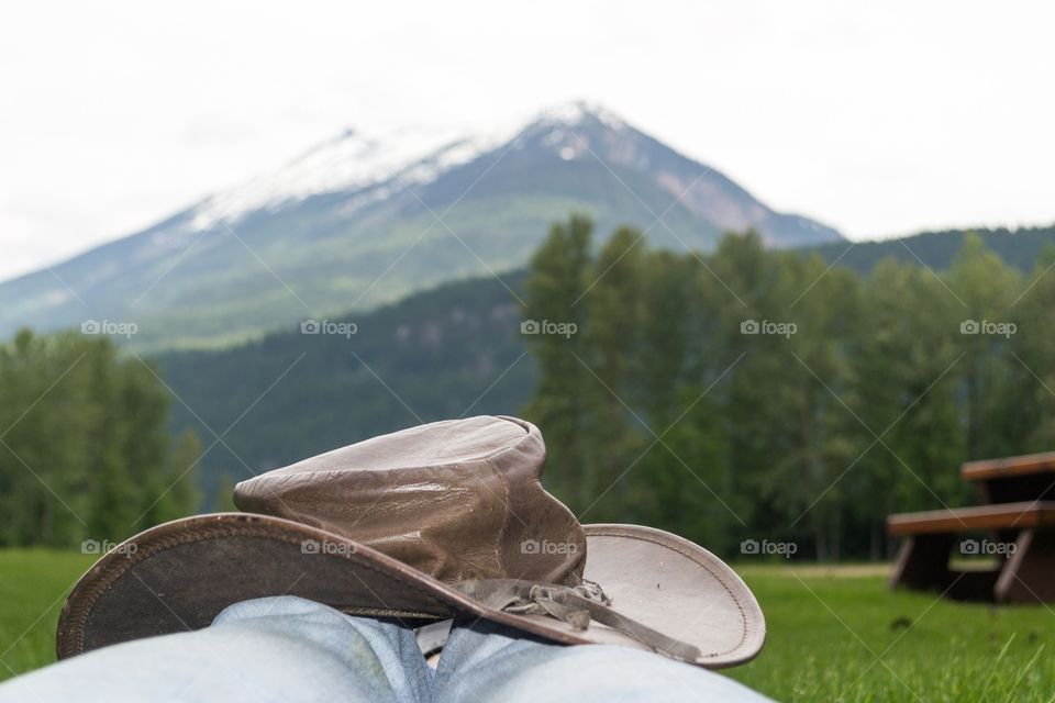 Cowboy taking in the view of one of Canada's Rocky Mountains from the vantage point of an alpine meadow, here resting with leather hat on knees 