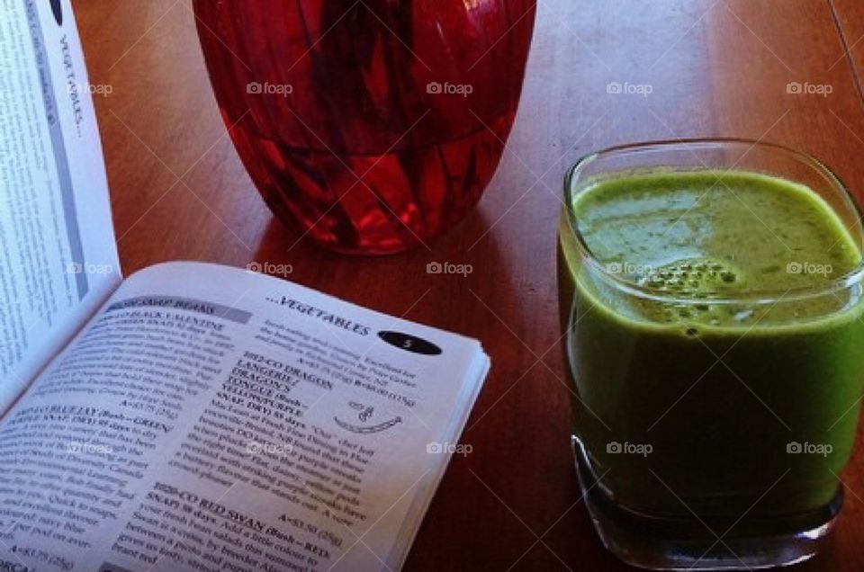 Green juice smoothie, vegetable seed catalogue. Red vase on wooden table 