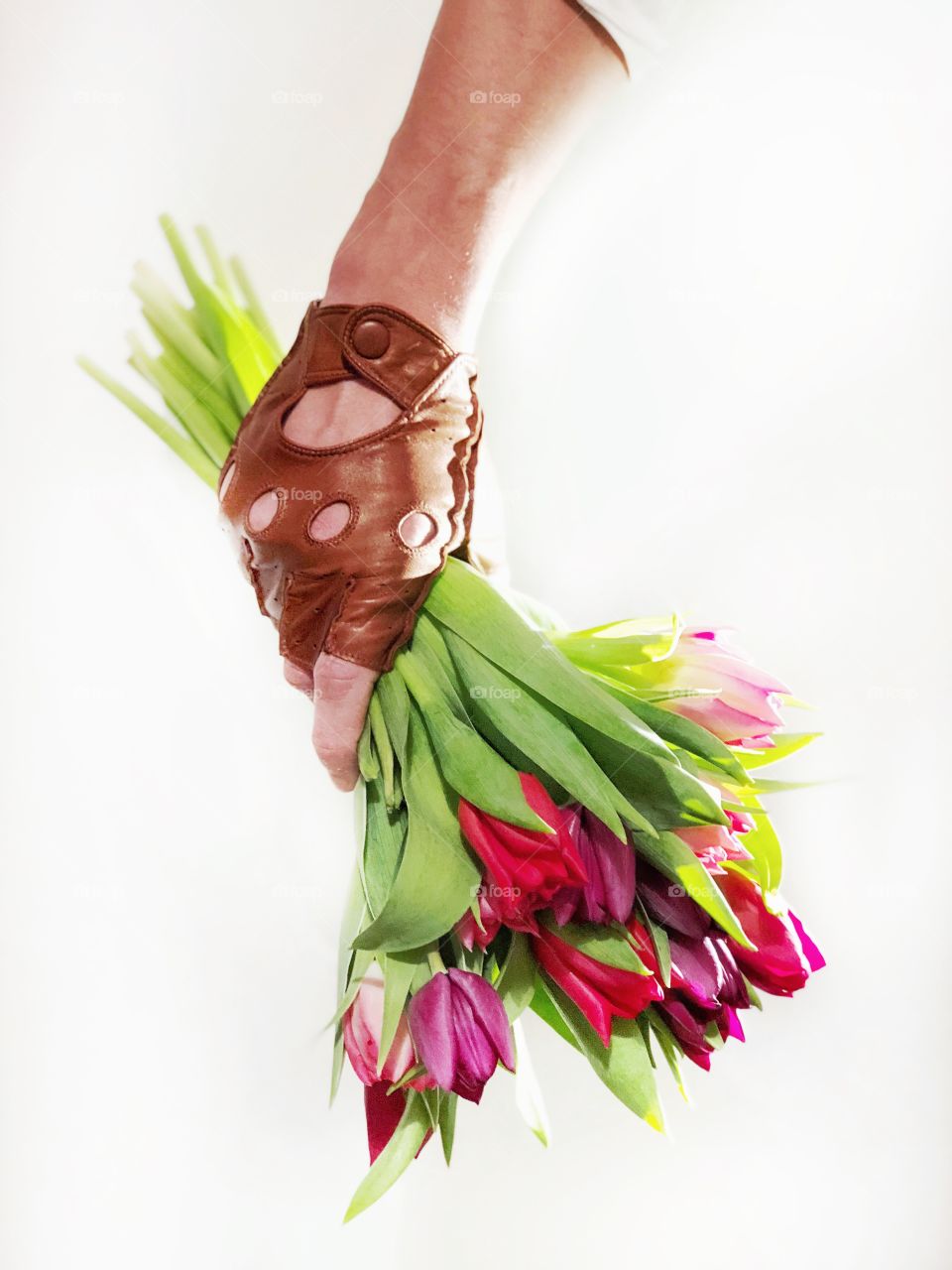 Men's hand in a glove holds a bouquet of colored tulips.