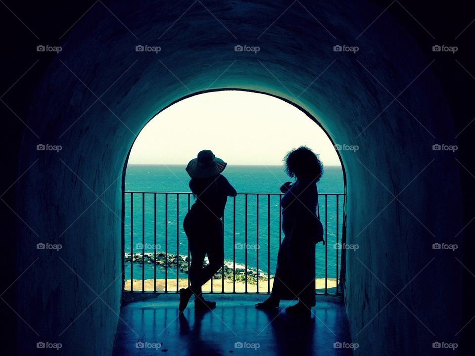 Silhouette. Two ladies at a window in El Morro overlooking the fort and ocean.