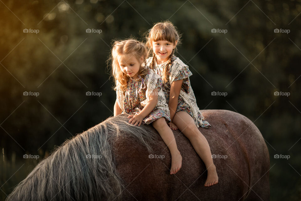 Little sisters on horse at summer evening 