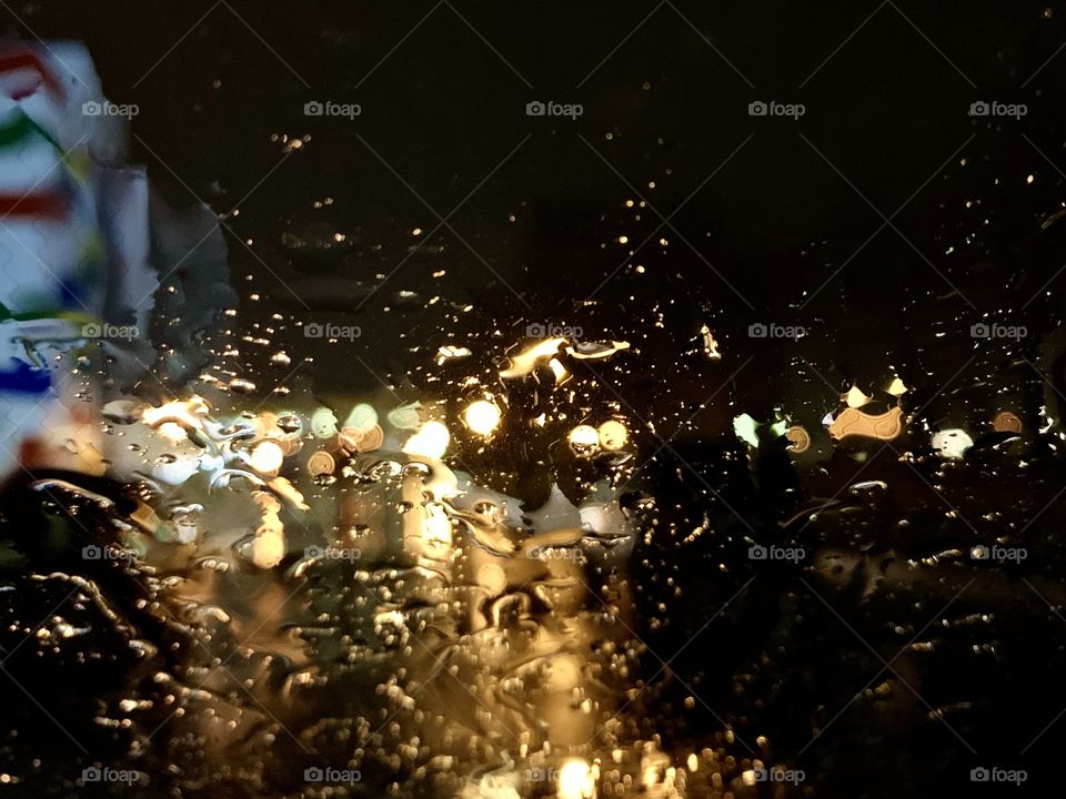 The lights of the night city are visible through a window wet from rain