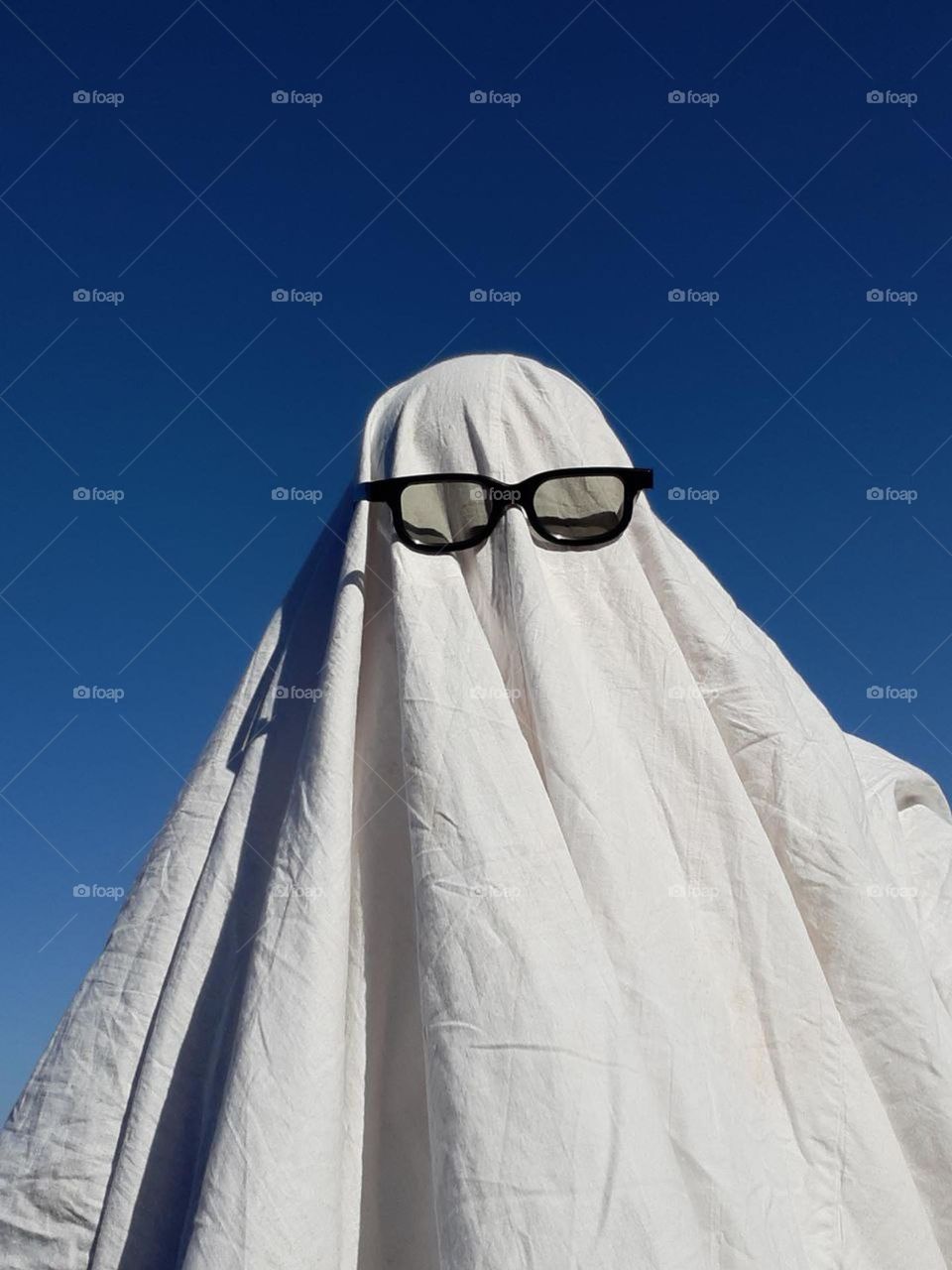 funny portrait of a man in the image of a ghost in sunglasses against a clear blue sky