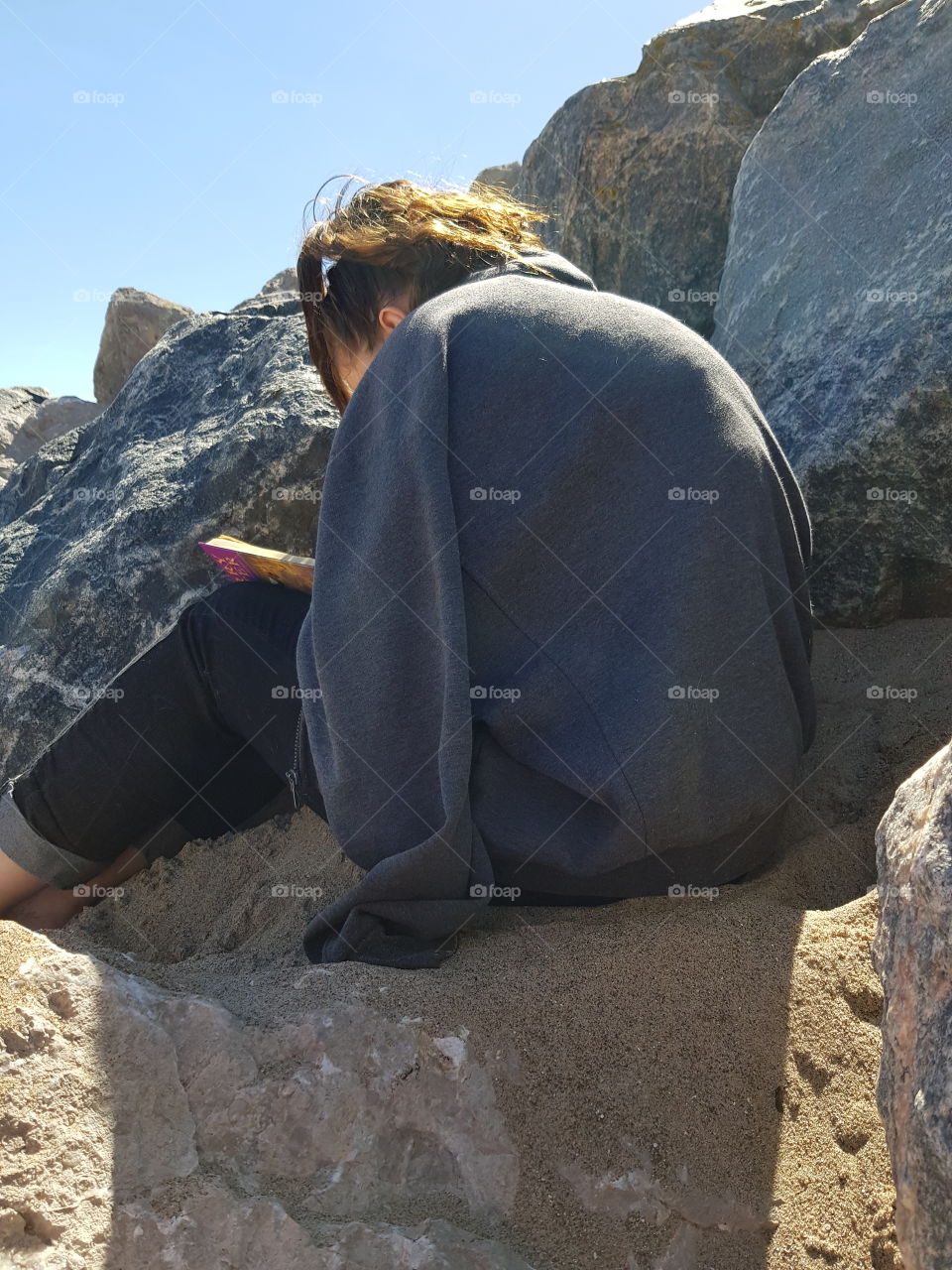 Girl between grey rocks reading on the sand